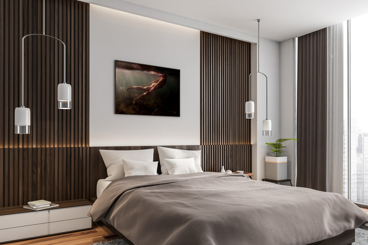 A contemporary bedroom features a spacious bed adorned with elegant gray bedding. Behind the bed, wooden paneling enhances the wall's aesthetic, while a framed artwork titled "Blush 03" by Francesca Owen, printed with archival pigments on fine art paper and accompanied by a certificate of authenticity, hangs prominently above. Beside the bed, two pendant lights add to the ambiance as natural light pours in through tall windows offering stunning cityscape views.