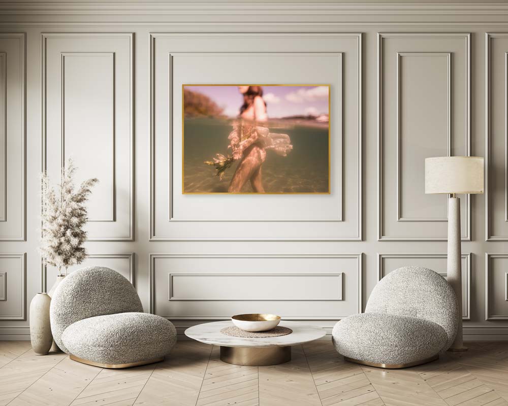 A modern, elegantly designed living room features light green panelled walls, two round grey fabric chairs, a low round coffee table, a large dried floral arrangement, and a floor lamp. Centrally hanging on the wall is *The Language of Flowers #1* by Francesca Owen—an exquisite framed image of a woman in water, printed on fine art paper with archival pigments for lasting beauty.