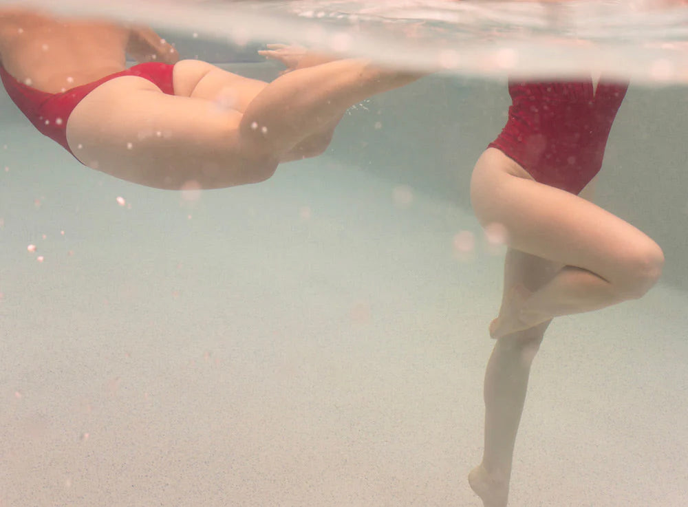 “Opposites Attract 02” by Francesca Owen features two people in red swimsuits partially submerged in a pool, radiating tranquility and clarity—ideal for fine art paper prints.