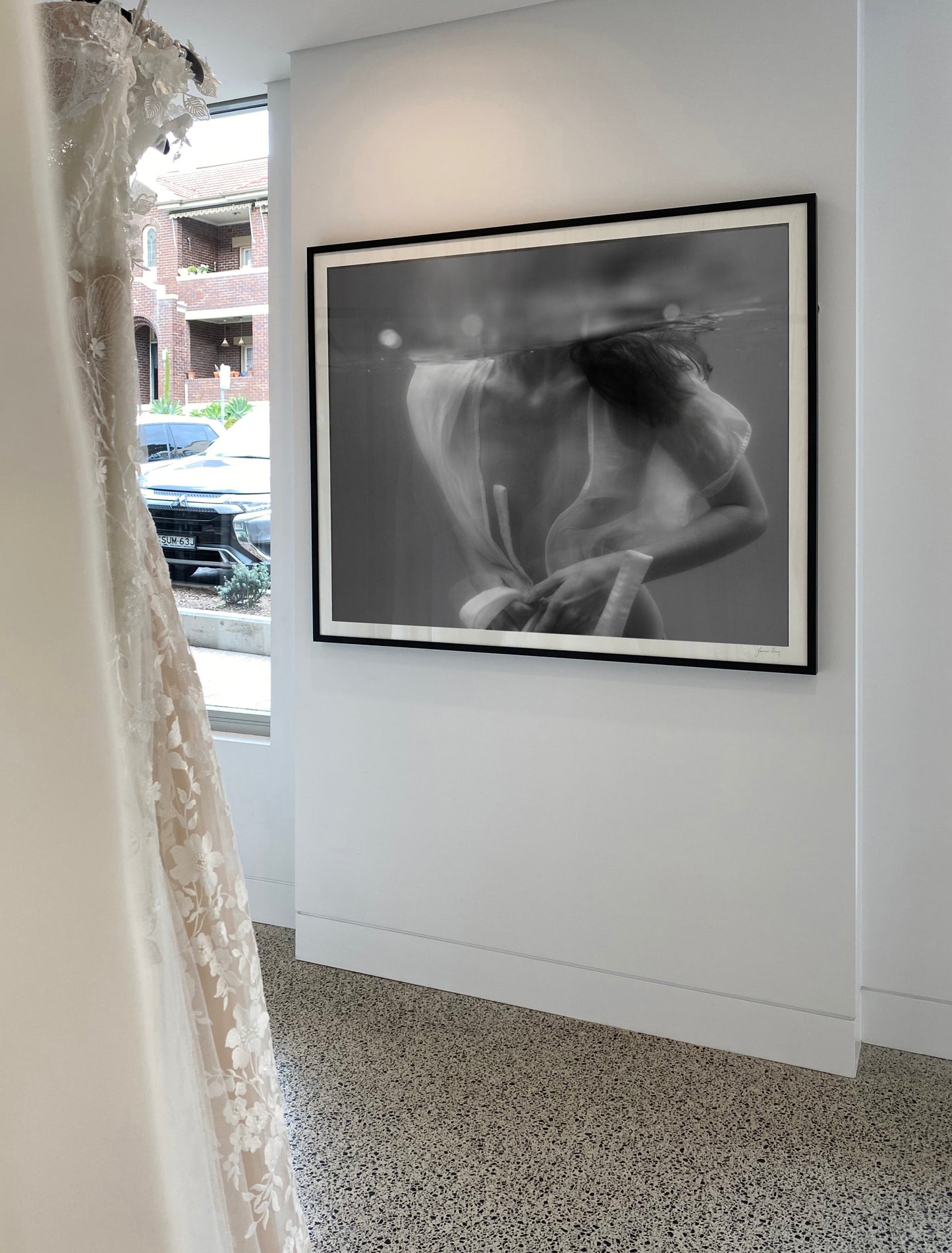 The intriguing black and white underwater photograph, titled "Softness #1 B&W" by Francesca Owen, captures a person partially submerged in water wearing an unbuttoned, translucent white shirt. With their head above the water's surface and their torso and hands below, the image creates an ethereal and serene atmosphere ideal for fine art prints or custom framing.
