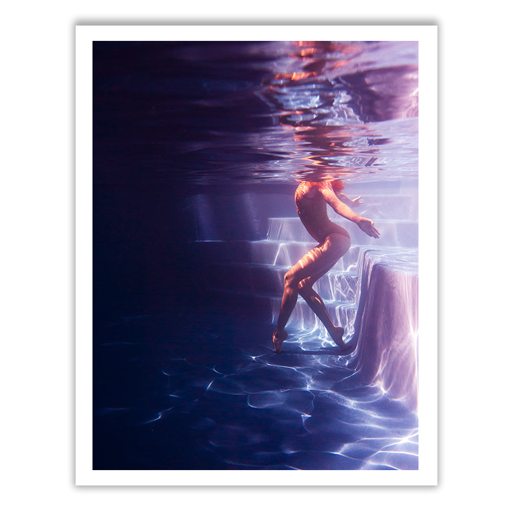 A figure submerged beside a pool ladder, softly illuminated to evoke a serene and ethereal atmosphere. The individual seems to float gracefully with outstretched arms amidst the water's reflective qualities. This captivating scene, titled "Glisten 06" by Francesca Owen, is rendered using archival pigments on fine art paper to ensure its enduring quality and longevity.
