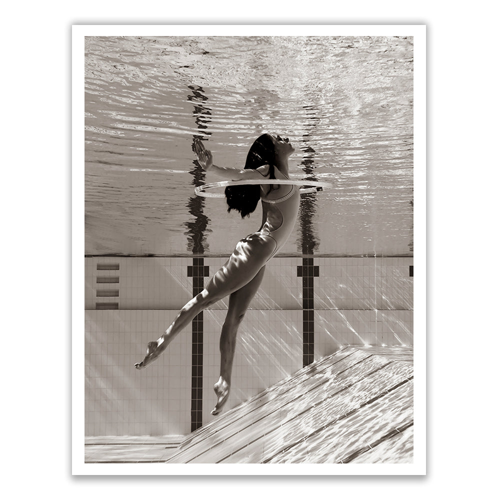 A black-and-white photograph titled "Flying Solo 01" by Francesca Owen features a woman wearing a one-piece swimsuit, partially submerged in a swimming pool. She gracefully extends her legs while keeping her head above the water's surface, with her reflection clearly visible. This fine art print utilizes archival pigments for lasting quality and comes with a certificate of authenticity.