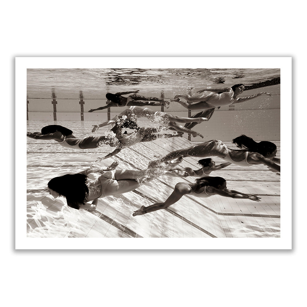 Ladies in Waiting #4" by fine art photographer Francesca Owen features a striking black-and-white photograph of underwater swimmers in synchronized motion, generating ripples and bubbles. The image captures several individuals in swimwear mid-stroke, with their reflections visible on the water’s surface and the tiled pool floor beneath them. This limited edition print is on Giclee fine art paper.