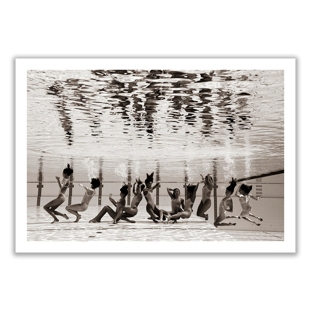 An underwater photo of a group of children swimming in a pool. The water's surface above them reflects their movements, creating a distorted mirror image. This black and white Fine Art Print, titled "Ladies in Waiting #5" by Francesca Owen, captures the playful and carefree essence of their activity perfectly.