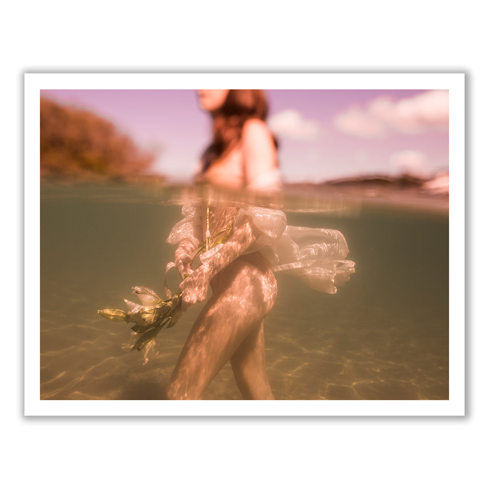 A submerged woman holding a bouquet of flowers stands waist-deep in water, with the upper part of her body above the waterline. The scene, printed on fine art paper with archival pigments, is bathed in warm, pinkish tones, capturing a serene and dreamlike atmosphere. This artwork, titled *The Language of Flowers #1* by Francesca Owen, comes with a certificate of authenticity.
