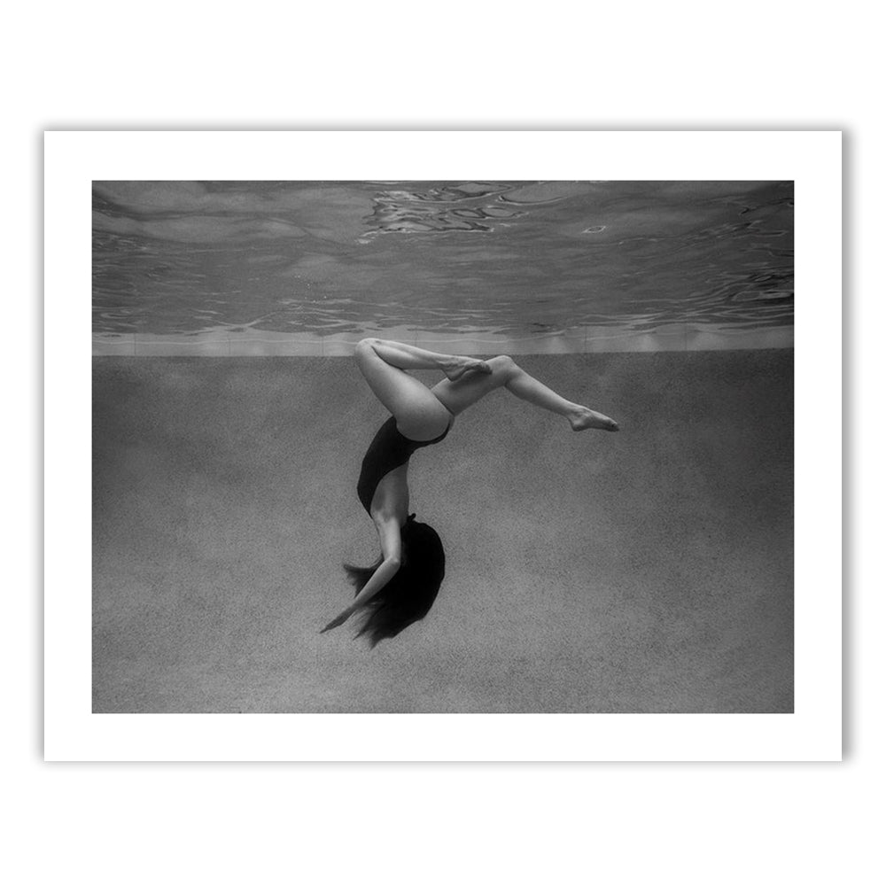 The "Palm Springs Solo" by Francesca Owen features a striking black-and-white image of a person underwater, positioned upside down with bent legs and extended arms. The person's long hair flows downward, enhancing the fluid motion captured in the photograph. This fine art piece is printed on premium archival paper using high-quality pigments and includes a certificate of authenticity.