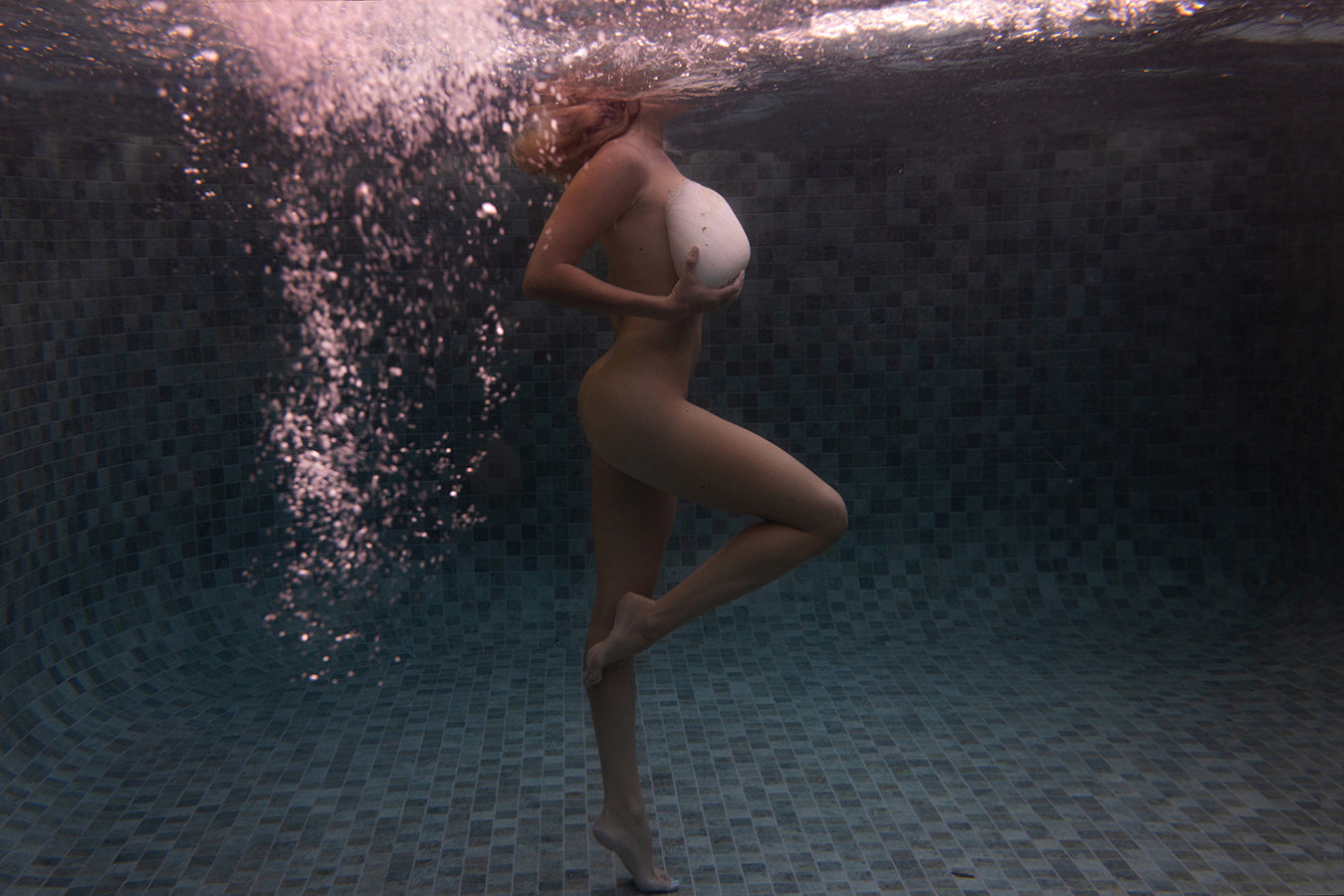 Shell & She #1 by Francesca Owen features a nude figure posing underwater on one leg, hands covering their chest, with light and bubbles moving over the tiled pool floor. This fine art print includes a certificate of authenticity.