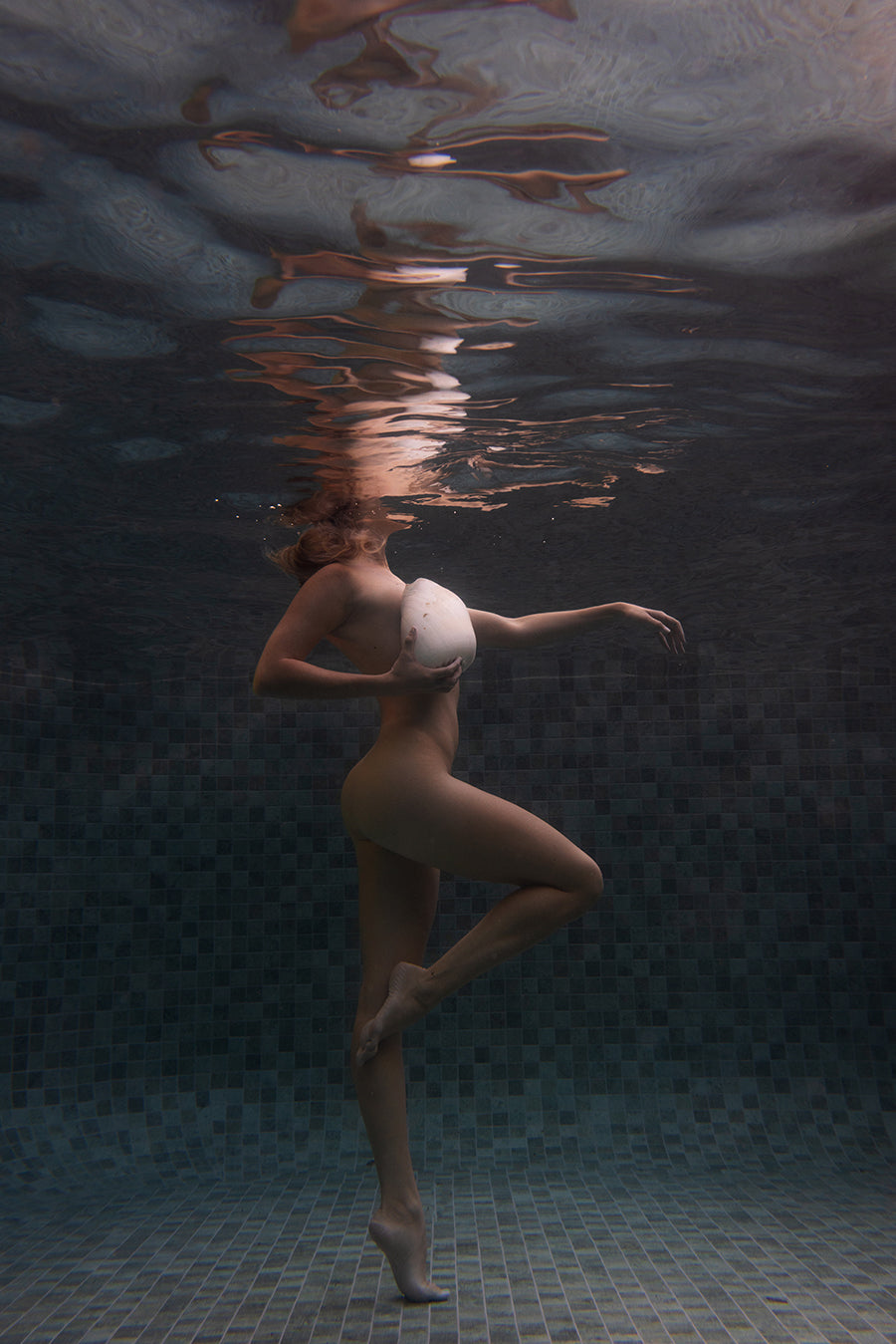 A person poses underwater in a tiled pool, one leg bent and arm raised gracefully, their head breaking the surface. "Shell & She" is a fine art print by Francesca Owen capturing this calm, artistic moment.