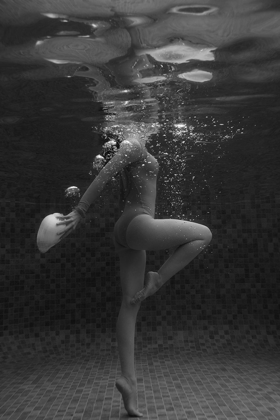 Shell & She #4 by Francesca Owen captures a person balancing underwater with a white cap, framed by shimmering tiles and bubbles. Available as a fine art print with certificate of authenticity.