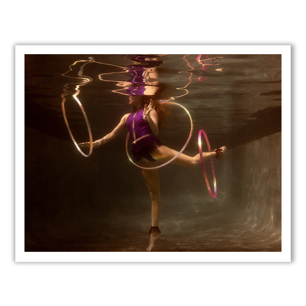 Show Time 2" by Francesca Owen depicts a figure in a purple swimsuit performing an underwater dance with three glowing hula hoops, set against a bronze-lit backdrop on fine art paper with archival pigments.