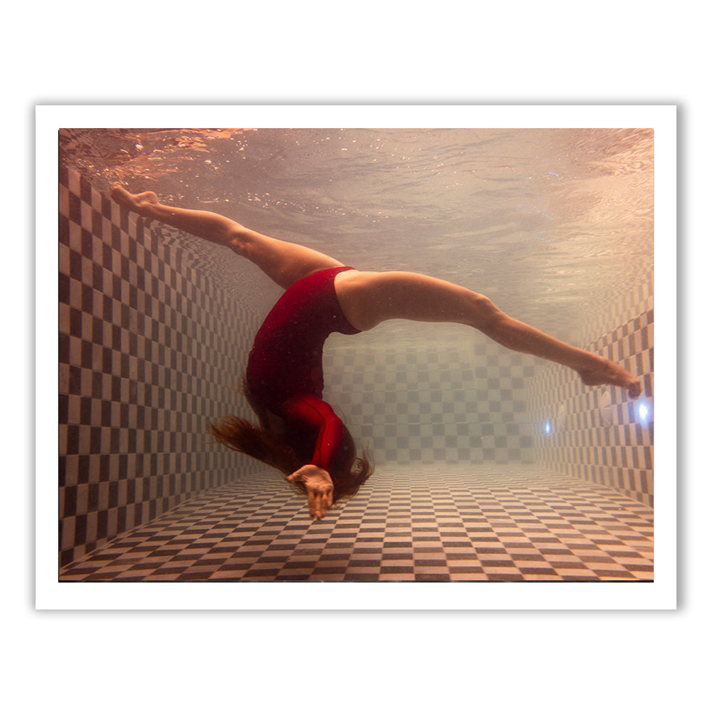 The fine art photograph, Wild at Heart no.4 by Francesca Owen, showcases a person in a red swimsuit performing a backbend underwater in a checkered pool. The water distorts the light, creating a unique visual effect and highlighting the elegance of the movement. Available for worldwide shipping, this image exudes serenity.