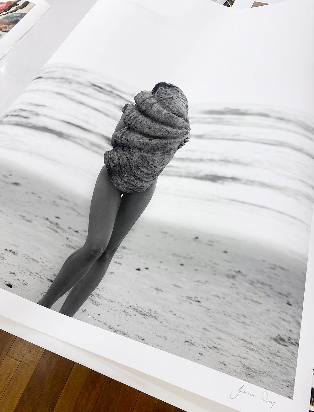 A black and white photo titled "The Beauty Within Part 2 #1" by Francesca Owen captures a person standing on a beach, facing away from the camera, wrapped in what appears to be a large piece of rope or textured fabric. Ocean waves roll gently in the background. This hand-signed image is printed on fine art paper, with worldwide shipping available.