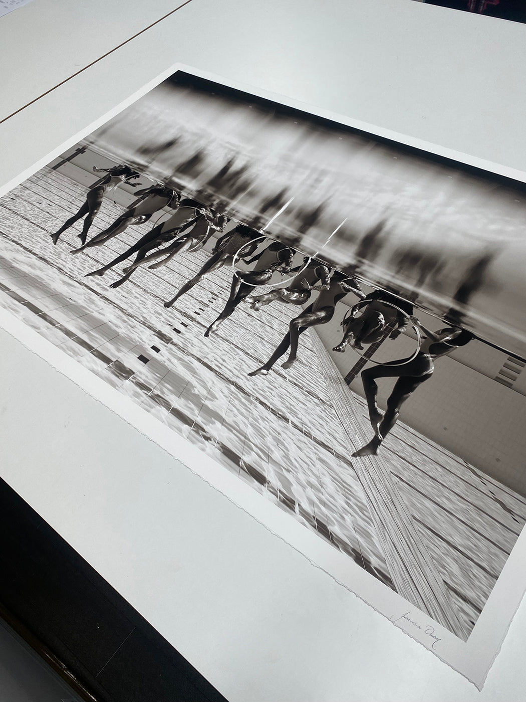 Francesca Owen's Ladies in Waiting #3 depicts a group of swimmers diving into a pool, captured mid-air just above the water's surface. This Limited Edition black-and-white photo, printed on Giclee fine art paper, accentuates dynamic action with reflections and movement.
