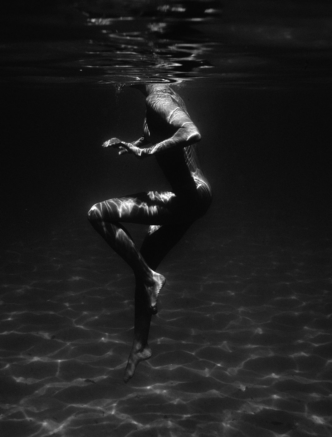 In "Still Waters #1" by Francesca Owen, a person, partially submerged, appears to be floating underwater in a graceful pose. The black and white image is printed on fine art paper using archival pigments, with light filtering through the water to create rippling patterns on the person's body. This ethereal scene comes with a certificate of authenticity.