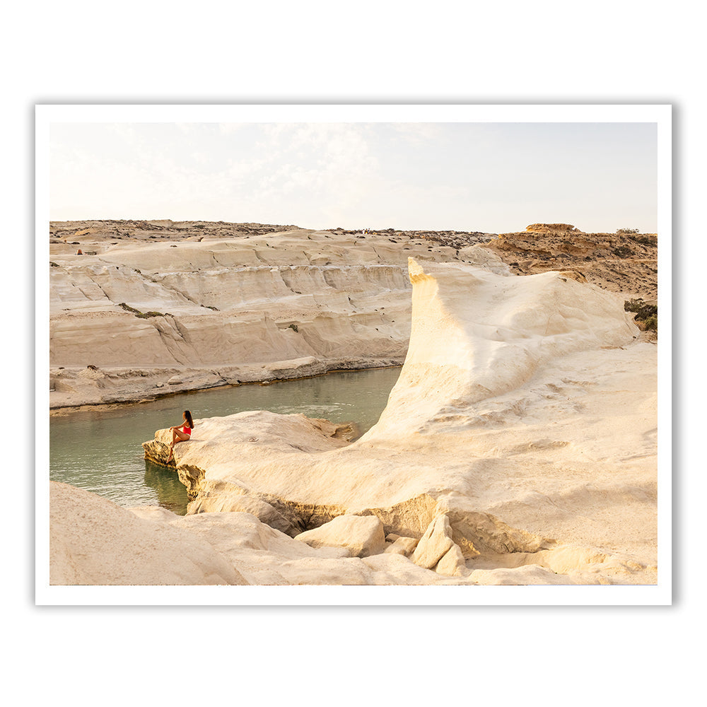 A person stands in the calm, clear waters of a natural pool surrounded by smooth, white rock formations, under a pale sky.