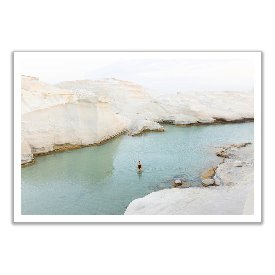 A lone swimmer in a pale green rock pool ringed by white cliffs in Milos