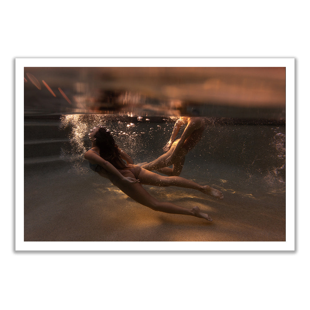 Two people in swimsuits float underwater in a swimming pool, with sunlight streaming in and air bubbles rising around them, creating a serene, dreamlike atmosphere.