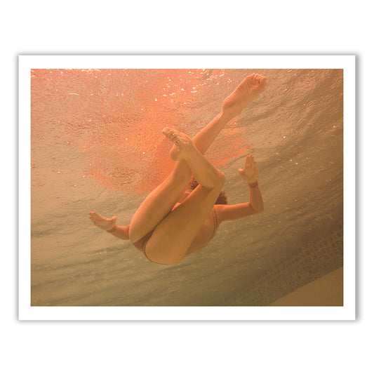 An underwater shot from Francesca Owen's "Another World," capturing a swimmer's legs and feet in an intricate, graceful pose just beneath the water's surface, bathed in warm, orange-tinted light. As part of our Limited Edition collection, these hand-signed photographs include worldwide shipping for your convenience.