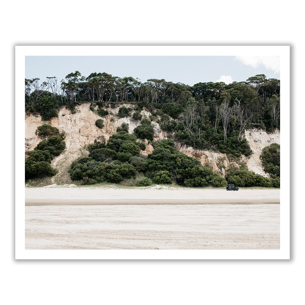 The photograph, titled "Australia #2" by Francesca Owen, depicts a sandy beach with sparse vegetation leading up to a cliff. The cliff is covered with bushes and trees at the top. A car is parked near the base of the cliff on the right side of the image, which has been captured using archival pigments for fine art prints. The sky is partly cloudy.