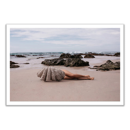 A person lies on a sandy beach, legs exposed and upper body hidden in a shell, in "The Beauty Within" by Francesca Owen—hand signed art prints printed in Australia.