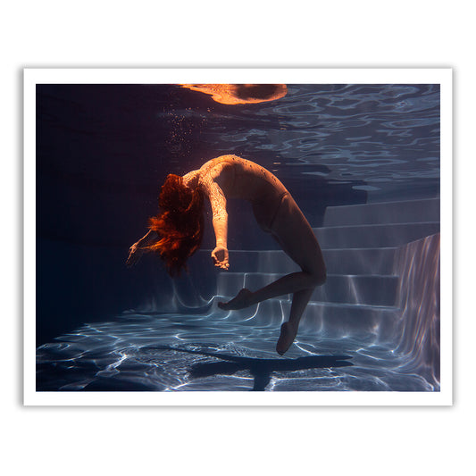 A person with long hair gracefully arches backward underwater in a swimming pool, creating subtle ripples and reflecting light to produce a serene and ethereal atmosphere. This enchanting moment, part of Francesca Owen's Glisten series, is titled "Glisten 02" and is available as fine art prints with worldwide shipping. The pool steps are visible in the background.