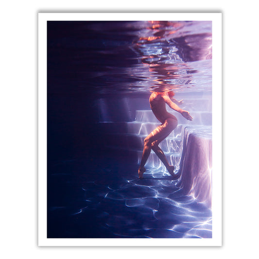 A figure submerged beside a pool ladder, softly illuminated to evoke a serene and ethereal atmosphere. The individual seems to float gracefully with outstretched arms amidst the water's reflective qualities. This captivating scene, titled "Glisten 06" by Francesca Owen, is rendered using archival pigments on fine art paper to ensure its enduring quality and longevity.