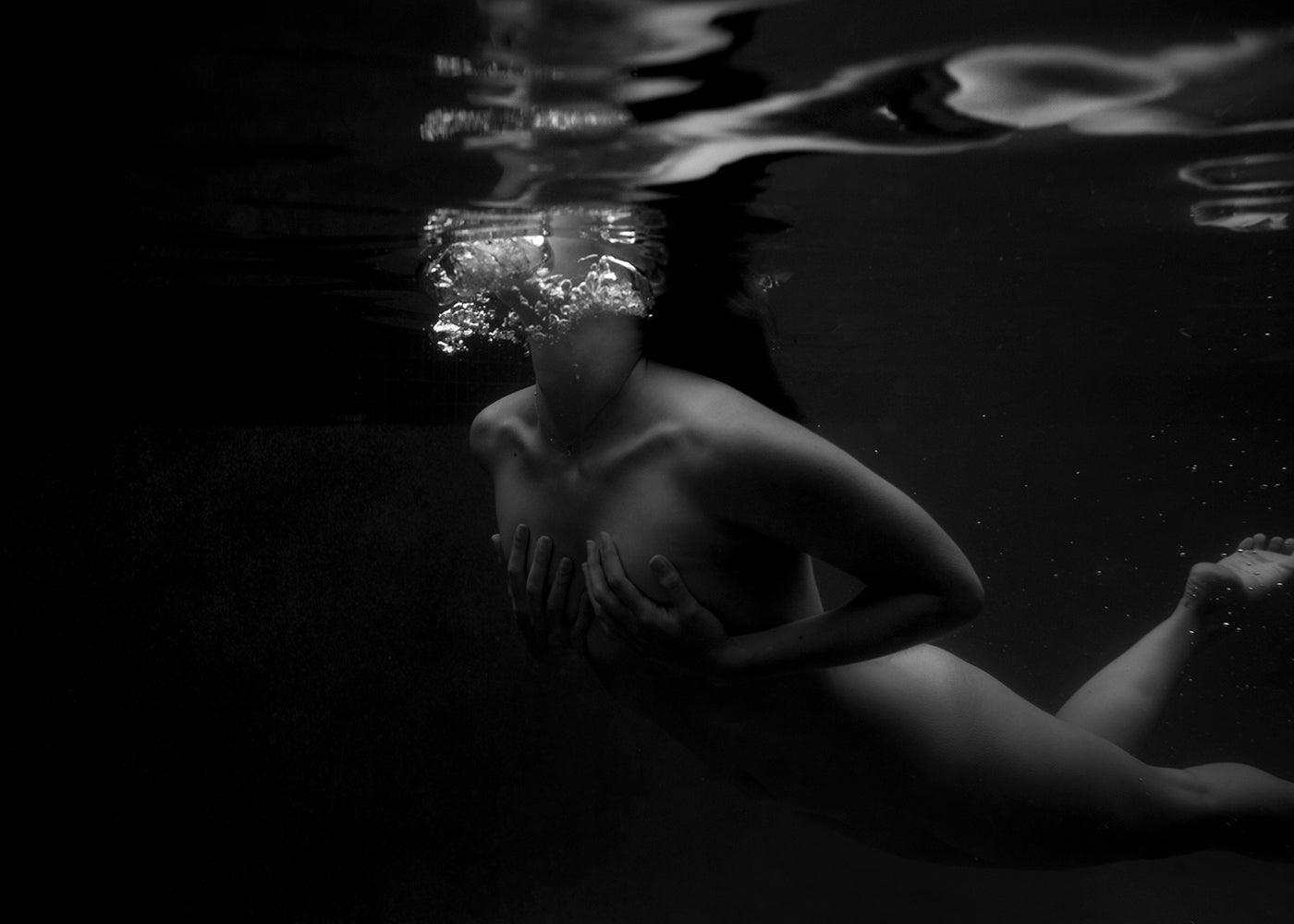 A black and white image titled "Hold On" by Francesca Owen depicts a person submerged in water, facing upwards with closed eyes. The person's hands touch their own upper torso, creating bubbles as they exhale. The water surface above is gently rippled with light reflections. This fine art print is available for worldwide shipping from Francesca Owen.