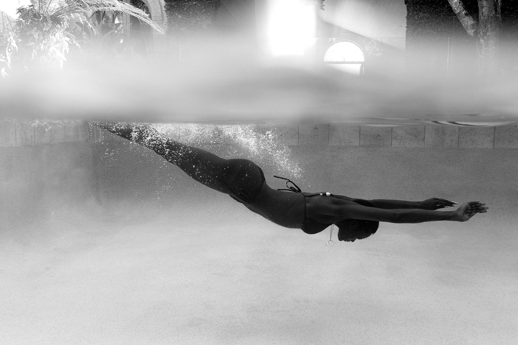 A black and white image of a swimmer in a bikini, streamlined with extended arms and legs, creates a bubble trail underwater in sunlight. Printed on fine art paper as Elegance #1 by Francesca Owen, it includes a certificate of authenticity.