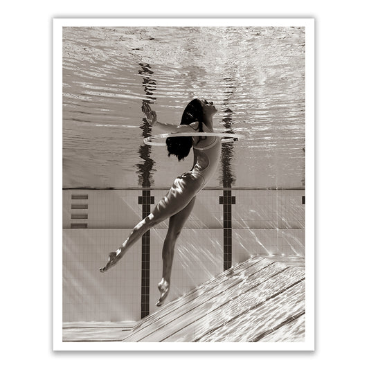 A black-and-white photograph titled "Flying Solo 01" by Francesca Owen features a woman wearing a one-piece swimsuit, partially submerged in a swimming pool. She gracefully extends her legs while keeping her head above the water's surface, with her reflection clearly visible. This fine art print utilizes archival pigments for lasting quality and comes with a certificate of authenticity.