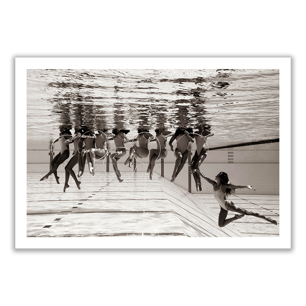 Ladies in Waiting #6" by Francesca Owen features a black and white underwater photo of synchronized swimmers. One swimmer is prominently performing a split in the foreground, while others form circular shapes in the background. Their reflections ripple on the water's surface above. This fine art photograph is available as a limited edition print on Giclee fine art paper.