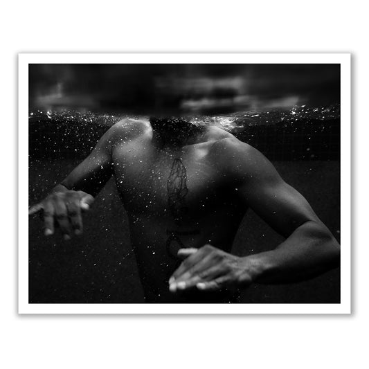Introducing "New Waters #2" by Francesca Owen: A captivating black and white photo of a person submerged underwater, visible up to their neck with only their torso in view. The individual's tattooed chest and the slightly out-of-focus effect enhance an ethereal, submerged ambiance. Hands extend as if swimming, adding to the evocative composition. Available as fine art prints with worldwide shipping.