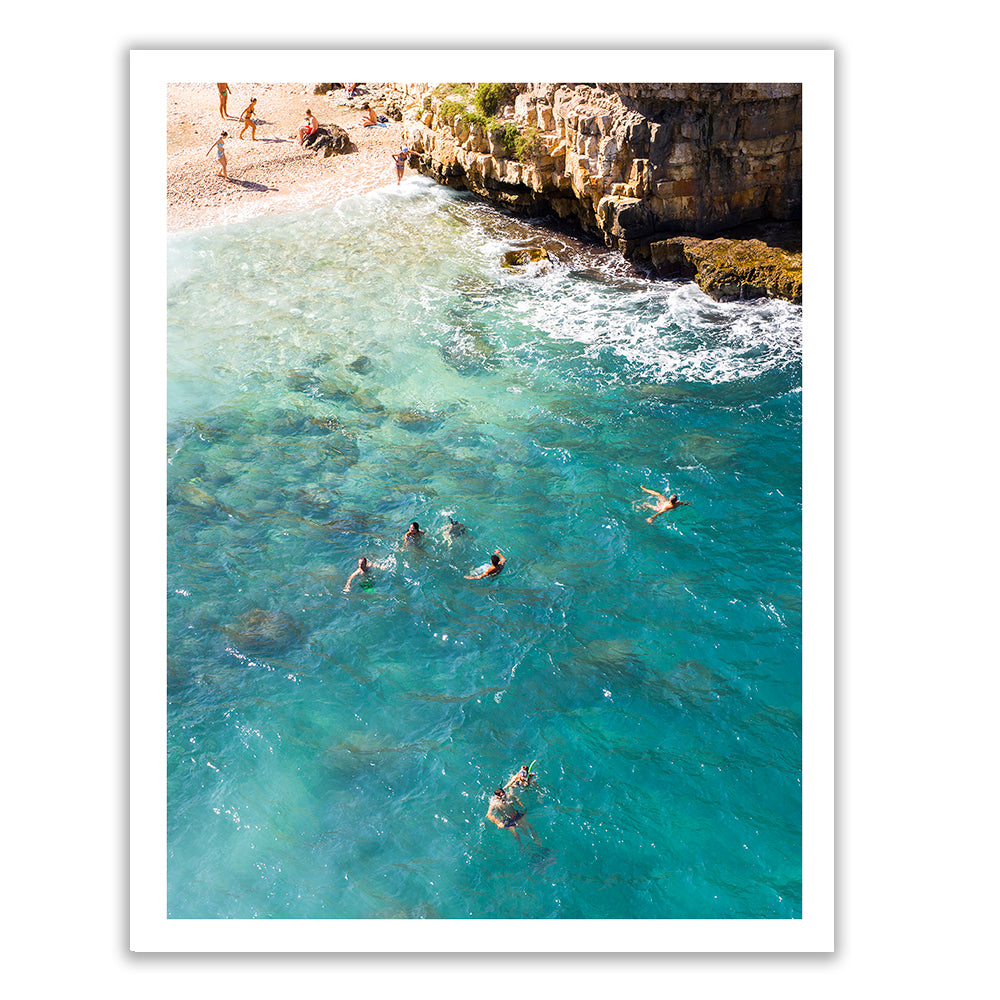 A large, vibrant photograph titled "A Polignano a Mare" by Francesca Owen captures people snorkeling in clear, turquoise waters near a rocky shoreline. The image, printed using archival pigments for lasting quality, is laid out on a white surface, possibly for display or framing. Fine art prints of this underwater beauty and beach scene are available with worldwide shipping.