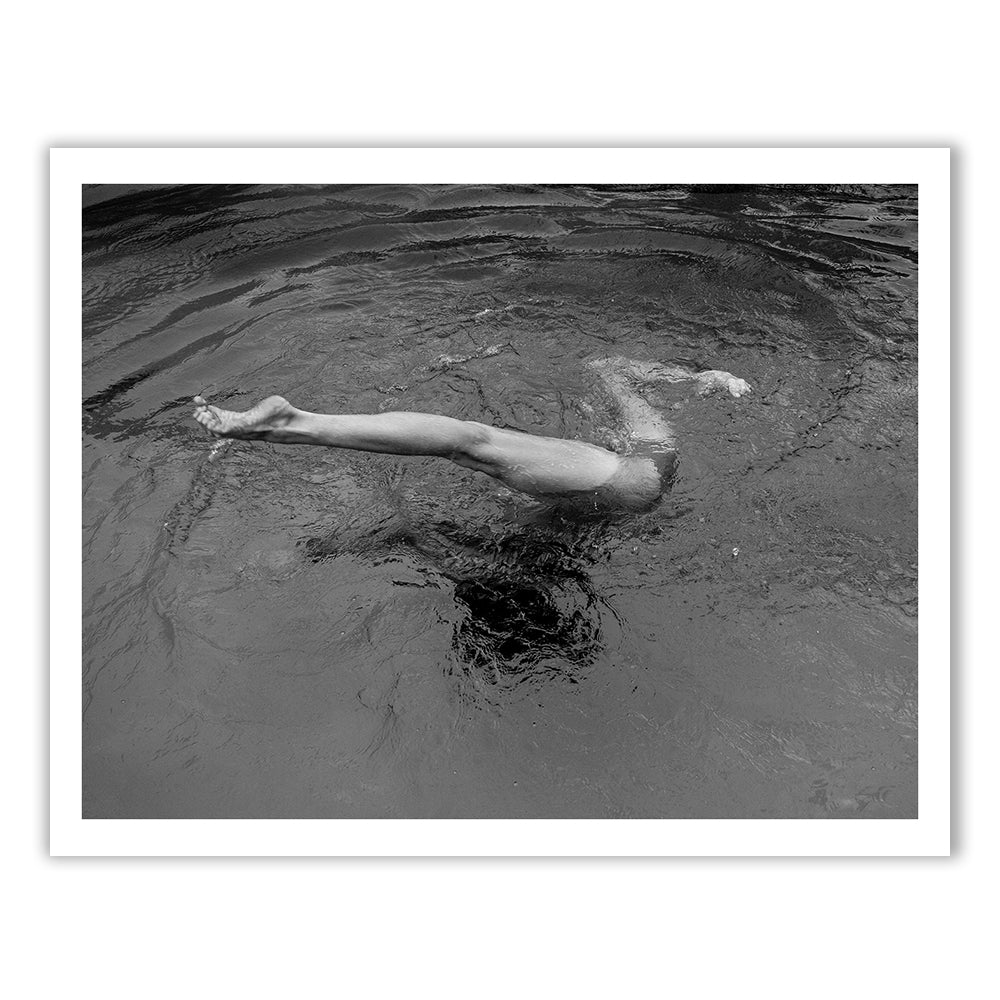 In "Red Head Series #7" by Francesca Owen, a striking black and white image captures a moment where a person dives into the water, their legs alone visible above the surface. The ripples around the diver create mesmerizing circular patterns, and this fine art print, produced using archival pigments for enduring quality, beautifully abstracts any details above the waist.