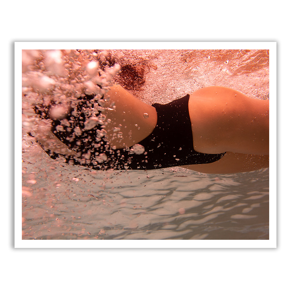 Underwater view of a person swimming, wearing a black swimsuit. Bubbles and water ripples surround them as they move through the water. The lighting creates a reddish hue in the scene, all captured beautifully in Francesca Owen's *Self Reflection 07*, rendered with archival pigments for depth and vibrancy.