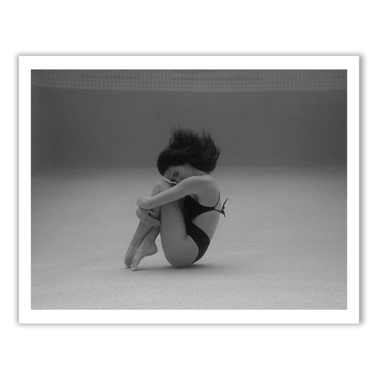Self Reflection 12 by Francesca Owen features a striking black and white photograph of a person in a swimsuit submerged underwater. The individual is curled into a ball with knees tucked to their chest, arms wrapped around their legs, while their hair floats freely. This exquisite piece is captured on fine art paper using archival pigments, and it comes with a certificate of authenticity.