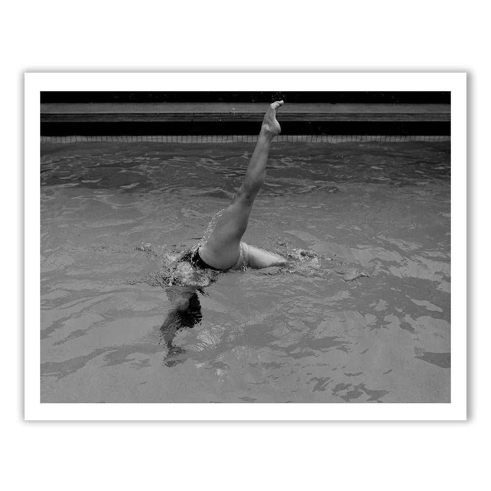 Self Reflection 19 by Francesca Owen features a black and white photo of a person in a swimming pool performing a vertical split, with one leg pointed straight up out of the water and the head submerged. Printed on fine art paper with archival pigments, this piece comes with a certificate of authenticity.
