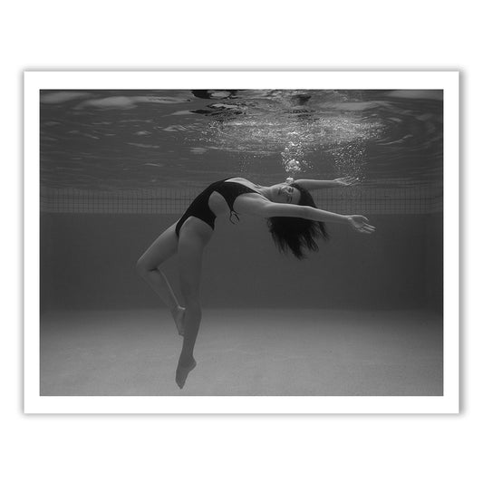 Self Reflection 02" by Francesca Owen features a black and white photo of a woman underwater, gracefully arching her body backward with her arms extended. She wears a one-piece swimsuit, surrounded by bubbles around her head. Printed on fine art paper using archival pigments, this image evokes a calm and serene atmosphere.