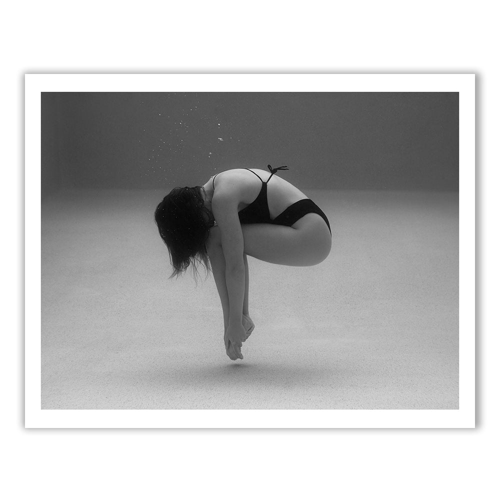 The artwork titled "Self Reflection 05" by Francesca Owen features a black and white photograph of a person underwater, curled into a fetal position. They are wearing a bikini, with their head down and arms reaching towards their feet. Bubbles rise above them in the clear water, revealing the sandy bottom. Printed on fine art paper using archival pigments, this piece comes with a certificate of authenticity.