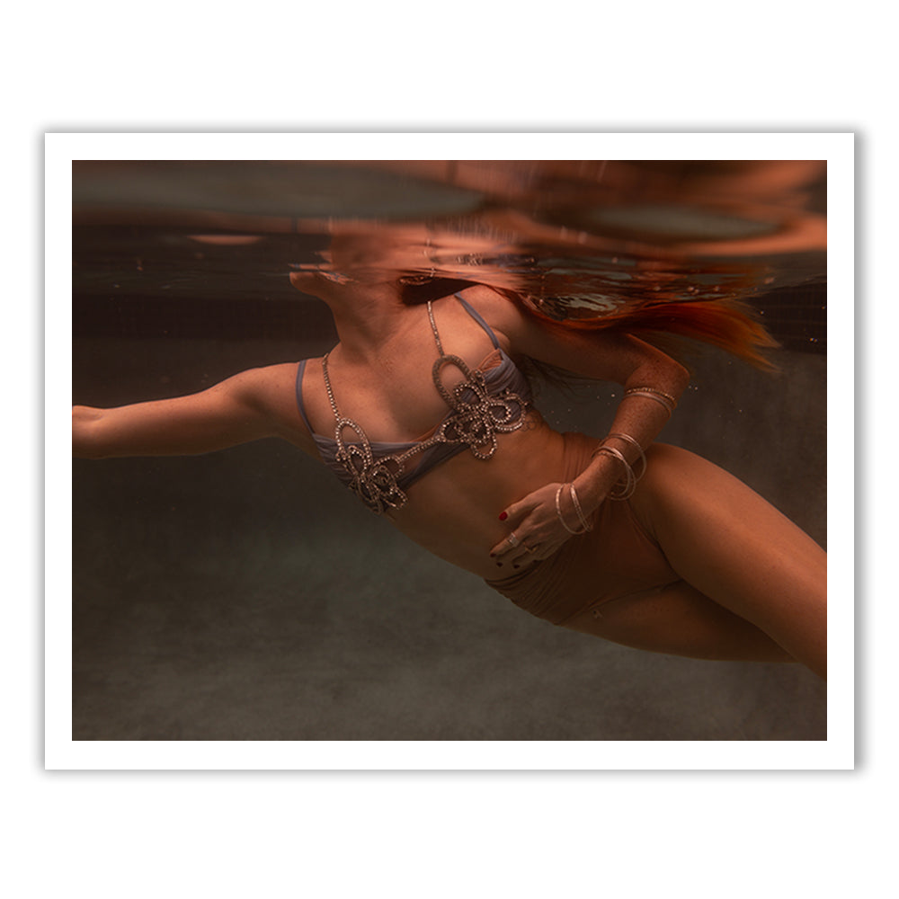 A person swims underwater in a tranquil pool, wearing Francesca Owen's Show Time Part 3, #8 top adorned with an intricate pattern. The light dances on the surface, creating reflections reminiscent of archival pigments found on fine art paper.