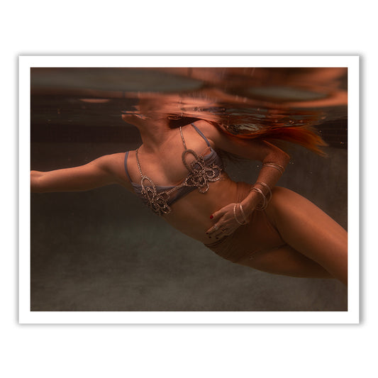 A person swims underwater in a tranquil pool, wearing Francesca Owen's Show Time Part 3, #8 top adorned with an intricate pattern. The light dances on the surface, creating reflections reminiscent of archival pigments found on fine art paper.