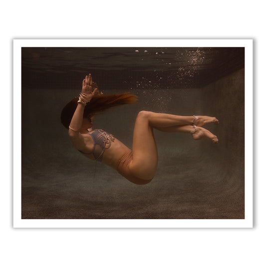 Underwater in a swimming pool, someone wearing the Francesca Owen "Show Time Part 3, #7" two-piece swimsuit seems to be part of an ethereal fine art piece. Floating gently in a fetal position, their hair streams upwards while bubbles dance around them, capturing a scene mirroring the precision of archival pigment on fine art paper.