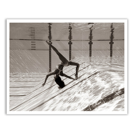 Flying Solo 04 by Francesca Owen features a sepia-toned photograph of a person in a one-piece swimsuit performing an elegant underwater pose in a swimming pool. The image, printed on fine art paper with archival pigments, captures the subject with one arm extended downward and one leg lifted while touching the pool floor, creating mesmerizing reflections on the water surface above. Each print comes with a certificate of authenticity.