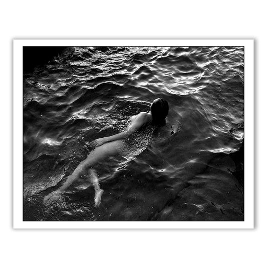 The black-and-white photograph, titled "Sunrise Swim #1" by Francesca Owen, printed on fine art paper, depicts a person swimming naked in dark, rippling water. The figure is partially submerged and moving leisurely. The water's texture and light reflections create a serene, yet somewhat mysterious atmosphere. Worldwide shipping available with a certificate of authenticity.