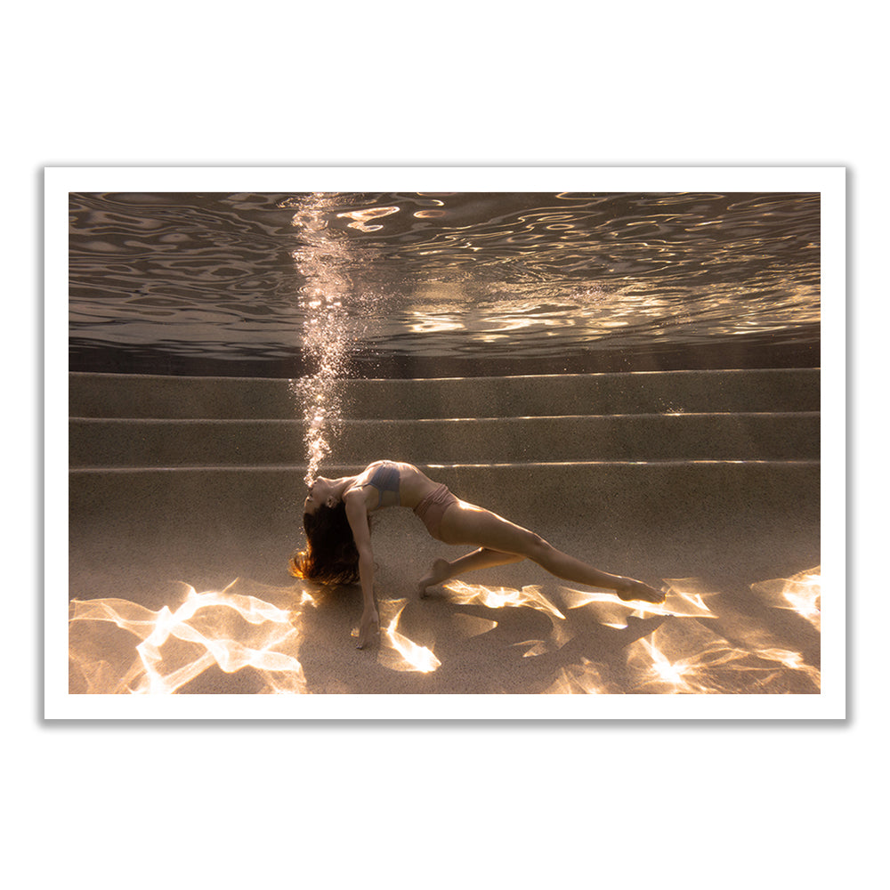 A woman in a swimsuit arches backward underwater on pool steps, exhaling bubbles, as sunlight shimmers below. "Sunset #2" is a fine art print by Francesca Owen, available with a certificate of authenticity.