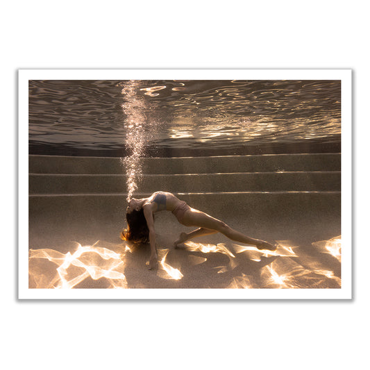 A woman in a swimsuit arches backward underwater on pool steps, exhaling bubbles, as sunlight shimmers below. "Sunset #2" is a fine art print by Francesca Owen, available with a certificate of authenticity.