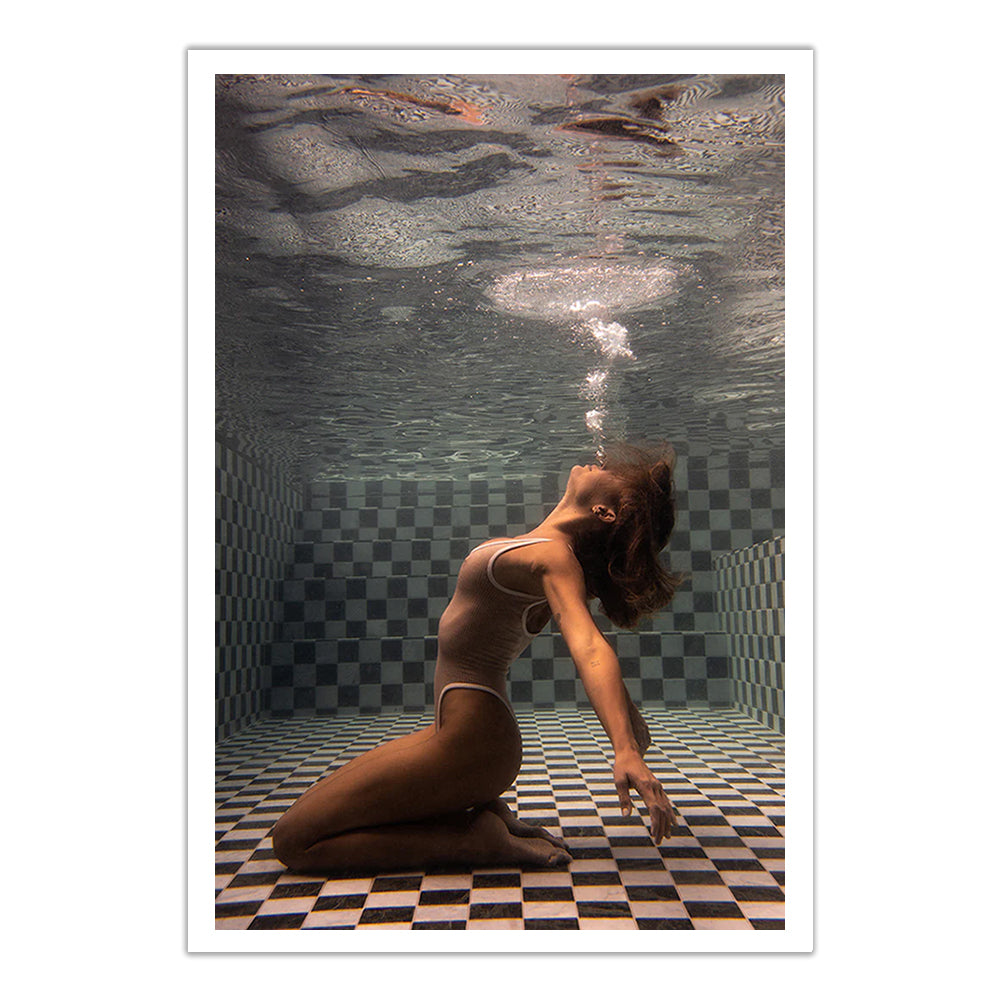 A woman in a swimsuit kneels on a checkered pool floor underwater, arching her back and blowing bubbles—"The Banya #1," a stunning fine art print by Francesca Owen, available with a certificate of authenticity.