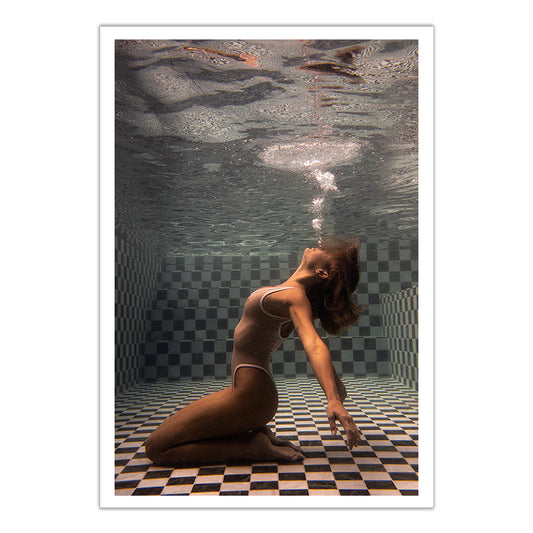 A woman in a swimsuit kneels on a checkered pool floor underwater, arching her back and blowing bubbles—"The Banya #1," a stunning fine art print by Francesca Owen, available with a certificate of authenticity.