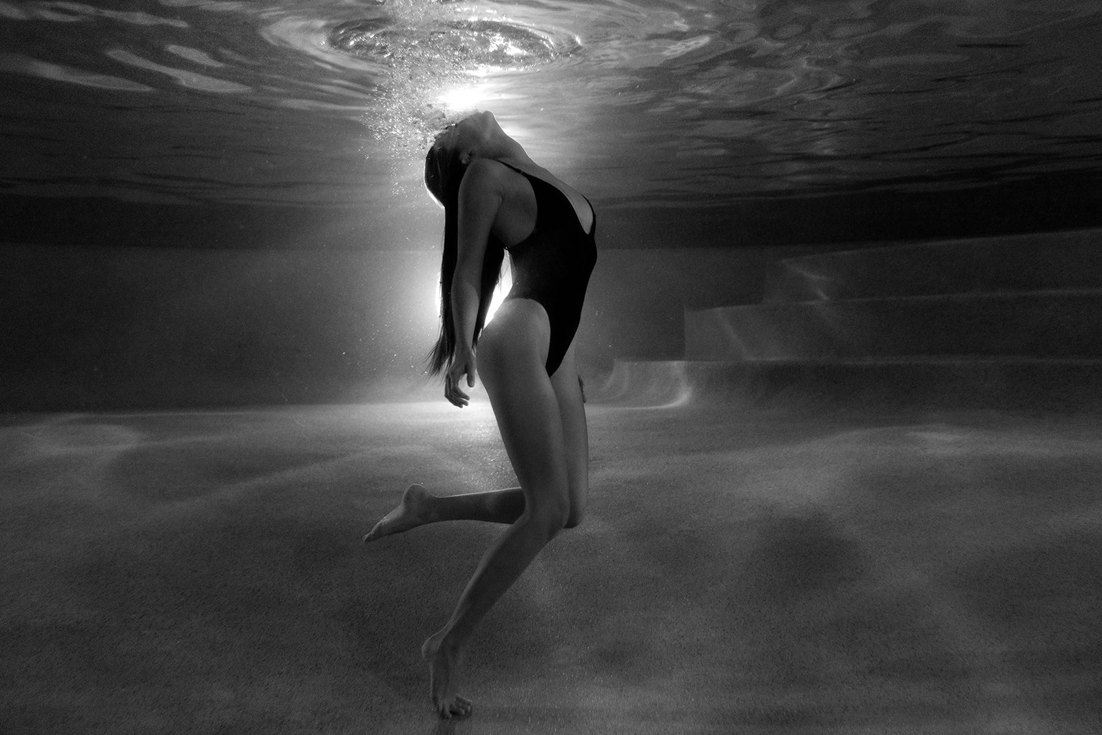 A woman in a swimsuit arches gracefully underwater amid rising bubbles in this serene black-and-white scene, available as "The Bower #4 B&W" fine art print by Francesca Owen, complete with a certificate of authenticity.