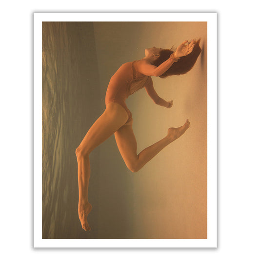 A person in a red swimsuit, appearing to dance underwater with a gracefully arched body and flowing hair, is captured against a serene gradient from blue to beige in "The Resistance" by Francesca Owen. This Limited Edition artwork is printed using archival pigments on fine art paper and comes framed with a white border.