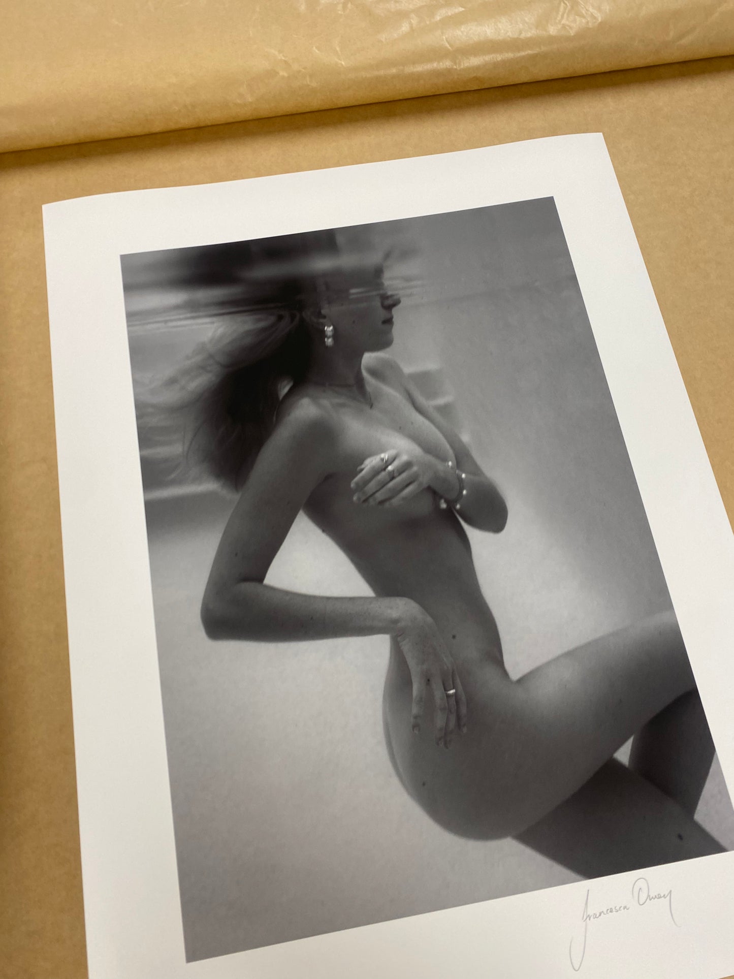 Unveiled 02" by Francesca Owen captures the allure of a nude subject submerged underwater with their face partially visible. The long hair floats ethereally in the water, and the subject is adorned with earrings. This black-and-white photograph, rendered using archival pigments, is printed on fine art paper to ensure its exquisite detail and depth are meticulously preserved.